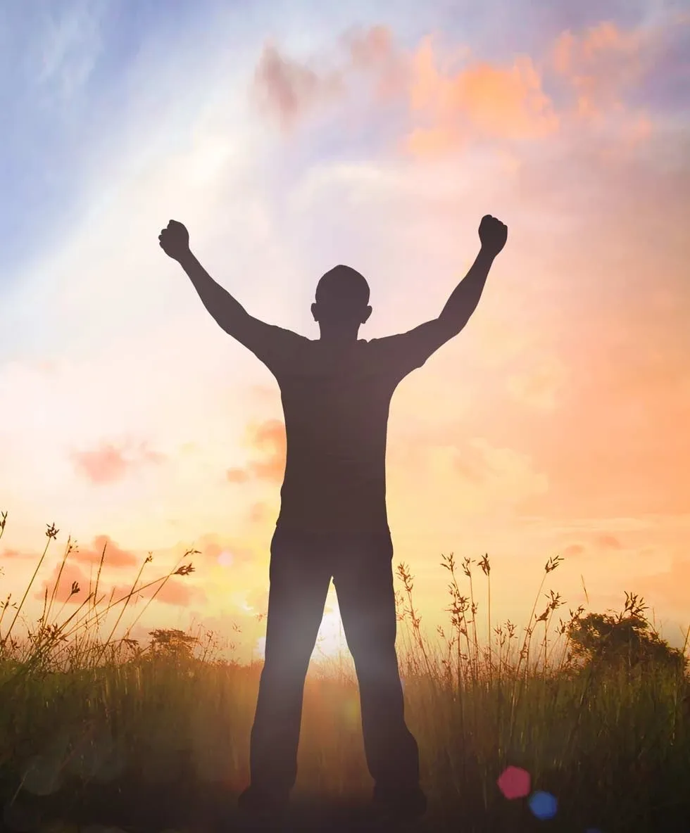 A man standing in the grass with his arms raised.